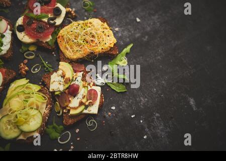 Vielfalt an gesunden frischen Sandwiches mit verschiedenen Gemüse, Kräutern und Zutaten auf dunklem Tisch Stockfoto