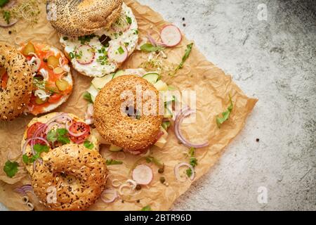 Leckere bunte Bagels mit gesunden Zutaten auf braunem Backpapier serviert Stockfoto