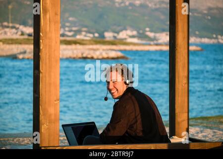 Ein Mann, der Laptop und Headset im Freien am Strand benutzt Stockfoto