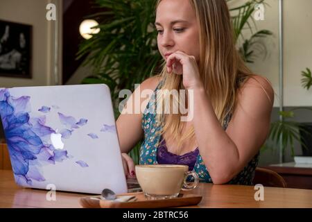 Eine Frau, die an einem Laptop arbeitet, mit einer Tasse Kaffee in einem Home Office oder Café Stockfoto