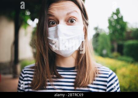 Ein blondes Mädchen, das draußen auf dem Land eine medizinische Schutzmaske trägt, mit dem abgestreiften Oberteil Stockfoto