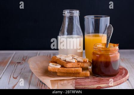 Zwei leckere Toasts mit gesalzenem Karamell und Bananen auf dem Tisch. Ein gesundes Frühstück mit Milch. Stockfoto