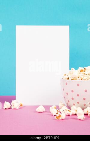 Frisches Popcorn in einer weißen rosa Schale auf rosa und blauem Hintergrund mit der leeren Papierseite Stockfoto