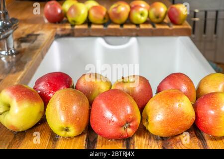 Nahaufnahme von Reihen von frischen, reifen, roten und grünen Äpfeln, die nach dem Waschen auf einem hölzernen Abtropfbereich um ein Spülbecken trocknen. Stockfoto