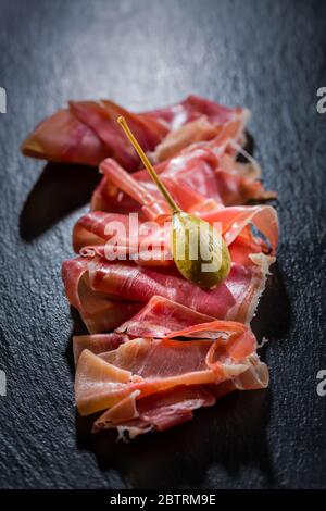 Köstlicher serrano-Schinken mit Kaperbeeren auf schwarzem Hintergrund Stockfoto