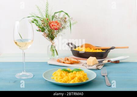 Risotto Mailänder, Holztisch mit traditionellem italienischen Safranrisotto, Gläsern und Krug Wein, Flasche Olivenöl, Korb mit Brot und Blumen Stockfoto