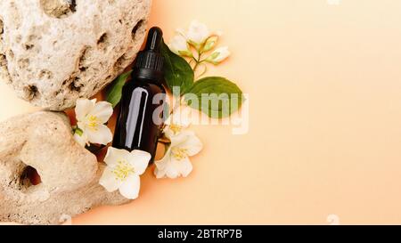 Schöne Komposition mit Teöl. Glas Kosmetikflaschen stehen auf einem Stein mit Jasmin auf einem beigen Hintergrund mit hellem Sonnenlicht. Naturkosmetik Konzept, natürliches ätherisches Öl Stockfoto