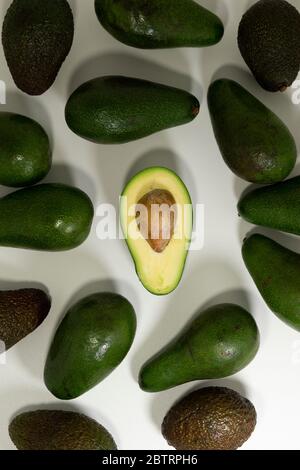 Ganze und in Scheiben geschnittene Avocado-Früchte mit einem sichtbaren Kern in der Mitte. Draufsicht Stockfoto