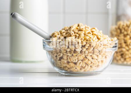 Gepuffter Weizen, der mit Honig bedeckt ist, in einer Glasschüssel. Frühstückszerealien auf dem Küchentisch. Stockfoto