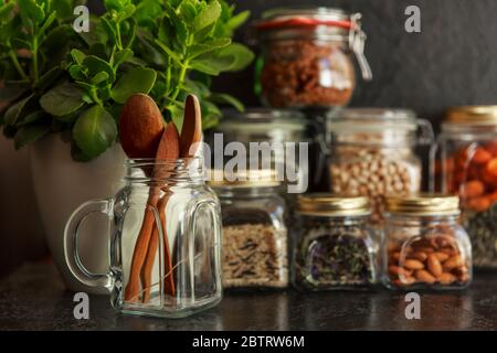 Speisenangebot. Rohes Getreide, Pasta, Grütze, Bio-Hülsenfrüchte und nützliche Samen in Gläsern. Vegane Quelle von Protein und Energieressourcen. Lagerung von Lebensmitteln in Gläsern, Öko-Shopping, auf dunklem Hintergrund, Zero Waste Storage Konzept, Recycling, Sustainable Lifestyle Concept Stockfoto