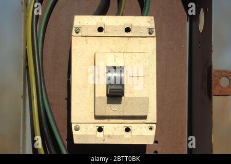 Ein alter elektrischer Schalter aus Kunststoff ist weiß in einem eisernen Kasten mit Drähten. Stockfoto