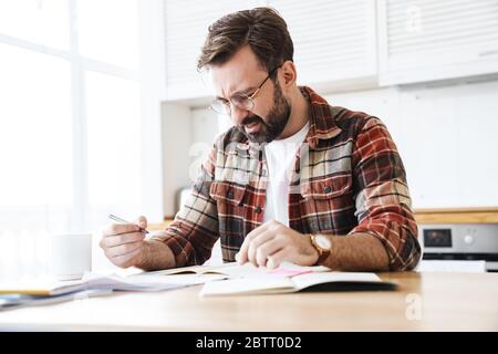 Porträt des jungen bärtigen unzufrieden Mann trägt Brille arbeiten mit Notizen zu Hause Stockfoto