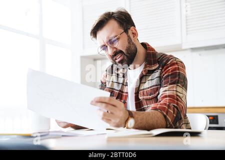 Porträt des jungen bärtigen unzufrieden Mann trägt Brille arbeiten mit Notizen zu Hause Stockfoto