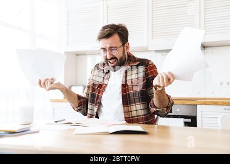 Porträt des jungen bärtigen unzufrieden Mann trägt Brille arbeiten mit Notizen zu Hause Stockfoto