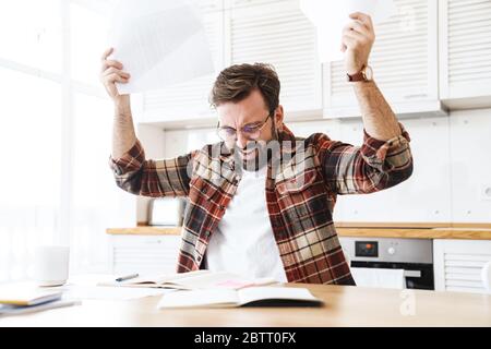 Porträt des jungen bärtigen unzufrieden Mann trägt Brille arbeiten mit Notizen zu Hause Stockfoto