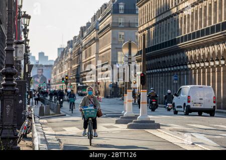 Paris, Frankreich - 14. Mai 2020: Junge Frau auf dem Fahrrad mit einer chirurgischen Maske, um sich vor Covid-19 in einer Pariser Straße zu schützen Stockfoto