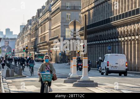 Paris, Frankreich - 14. Mai 2020: Junge Frau auf dem Fahrrad mit einer chirurgischen Maske, um sich vor Covid-19 in einer Pariser Straße zu schützen Stockfoto