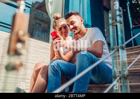 Gemischte Rennen Paar in der Liebe mit Smartphone zu Fuß in der Stadt. Arabischer Mann und weiße Frau, die Kaffee trinken und auf der Treppe sitzen Stockfoto