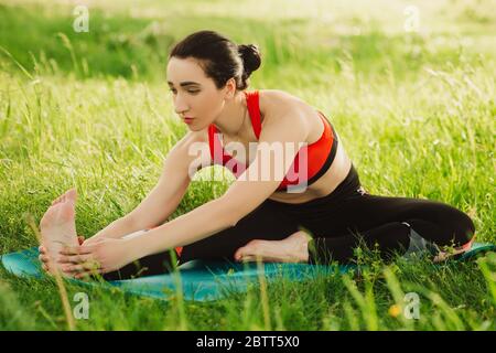 Junge Frau, die an sonnigen Tagen Yoga im Freien in der Natur auf dem Gras praktiziert. Outdoor-Sport. Übungen für Tonus, Flexibilität Stockfoto