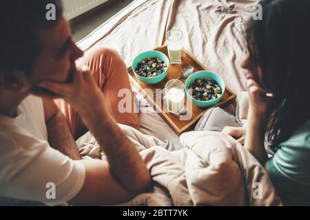 Ein reizendes Paar im Bett schaute sich an, bevor es morgens Müsli und Milch aß Stockfoto