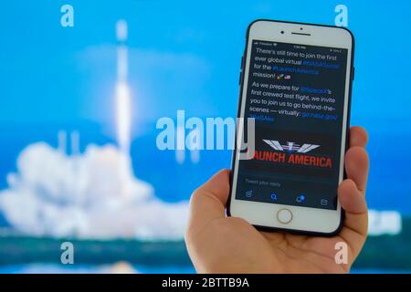 Kennedy Space Center, Florida, Usa. 27.Mai 2020. Eine Person, die ein iPhone mit dem Launch America Logo mit einem unfokussieren Raketenstart hält Stockfoto