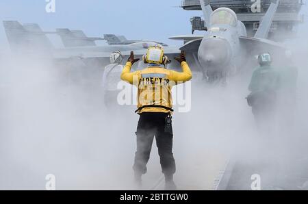 Der US Navy Aviation Boatswain Mate Airman Thomas McLaughlin leitet ein F/A-18E Super Hornet Jagdflugzeug, das den Dambustern von VFA 195 zugewiesen wurde, auf dem Flugdeck des Nimitz-Klasse Flugzeugträgers USS Ronald Reagan am 26. Mai 2020 in der Philippinischen See. Stockfoto