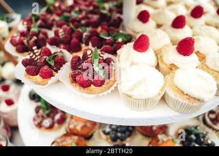 Köstliche Mini-Kuchen in Büfetts. Mit Himbeeren dekorierte Cupcakes. Verschiedene Desserts auf Party. Feier, Party, Geburtstag oder Hochzeit Konzept. Stockfoto