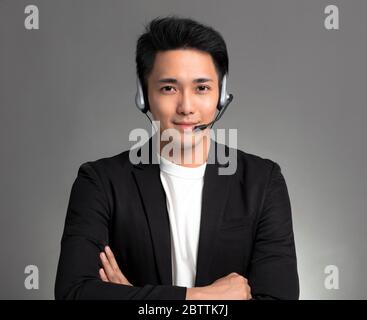 Lächelnd junge asiatische Geschäftsmann sprechen auf Headset vor grauem Hintergrund Stockfoto