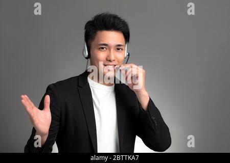 Lächelnd junge asiatische Geschäftsmann sprechen auf Headset vor grauem Hintergrund Stockfoto