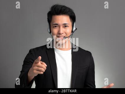 Lächelnd junge asiatische Geschäftsmann sprechen auf Headset vor grauem Hintergrund Stockfoto