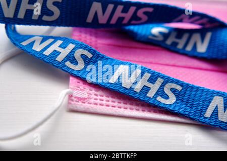 Große NHS-Buchstaben auf dem blauen Schlüsselband, das auf einer rosa antiviralen Gesichtsmaske angebracht ist. Konzept zur Bekämpfung der COVID-19-Pandemie. Stockfoto