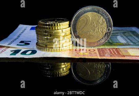 Stapel von Münzen, die neben einer 2-Euro-Münze auf einigen Euro-Scheinen gestapelt werden. Konzentrieren Sie sich auf Münzen. Stockfoto