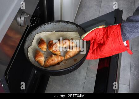 Mädchen Hand mit roten Schutzhandschuh nimmt Auflaufform mit gebackenen Brötchen aus dem Ofen in der Küche zu Hause Stockfoto