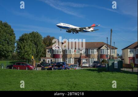 British Airways Boeing 747 landet am Flughafen Heathrow über Wohnhäusern an einem sonnigen Tag mit grünem Gras im Vordergrund. London. Stockfoto