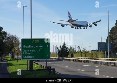 British Airways Boeing 747 landet am Flughafen London Heathrow über eine Autobahn mit einem Schild zum Flughafen im Vordergrund. Stockfoto