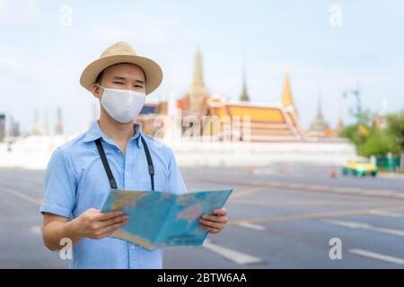 Asian Mann glücklich Touristen zu reisen mit Maske zum Schutz vor Covid-19 auf seinen Ferien und er schaut auf Reisekarte im Wat Phra Kaew Tempel in Bangk Stockfoto