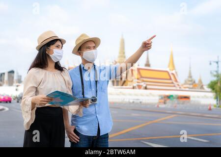 Asiatische Paar glücklich Touristen zu reisen tragen Maske vor Covid-19 zu schützen auf sie Urlaub und halten Reisekarte und zeigen in Wat Phra Kaew Temp Stockfoto