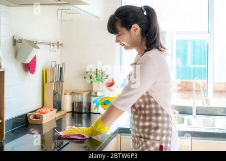 Asiatische Frau trägt Gummi Schutzhandschuhe Reinigung Küchenschränke in ihrem Haus während des Aufenthalts zu Hause mit Freizeit über ihre tägliche Haushälterin Stockfoto