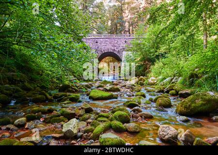 Der Geroldsauer fließt unter einer schönen grauen Steinbrücke, mit starkem Sonnenlicht im Hintergrund. Bühlertal, Deutschland Stockfoto