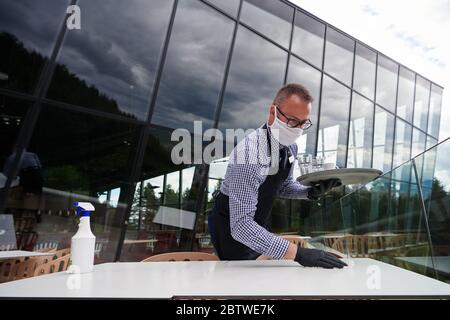 Kellner Reinigung der Tabelle mit Desinfektionsmittel Spray in einem Restaurant tragen medizinische Schutzmaske und Handschuhe neues normales Konzept Stockfoto