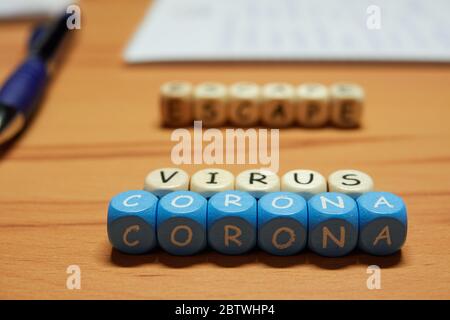 Blaue und braune Buchstaben bilden Würfel aus Holz. Die Wörter Corona Virus Escape im Hintergrund ist nützliches Büromaterial außer Fokus Stockfoto