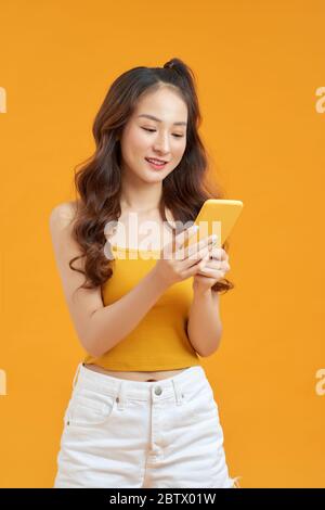 Foto von lustigen hübsche Dame halten Telefon Hände tragen weiße Tank-Top Jeans isoliert helle gelbe Farbe Hintergrund Stockfoto