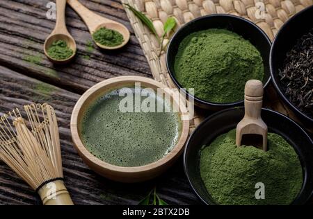 Japanisches Bio Matcha Grüntee Pulver in Schüssel mit Schneebesen und grünem Tee Blatt auf Holzhintergrund, Bio-Produkt aus der Natur für gesund Stockfoto