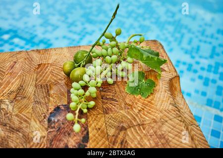 Frische grüne unreife Trauben, Mandarinen und Mangos auf einem Holzhintergrund in blauem Wasser und Kopierraum. Stockfoto