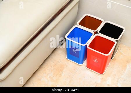 Müllklassifizierung Behälter in der Nähe eines Sofas in einem Salon zu Hause Englische Übersetzung für die lables-blau bedeutet recyclingfähige Müll, rot bedeutet schädlich, schwarz Stockfoto