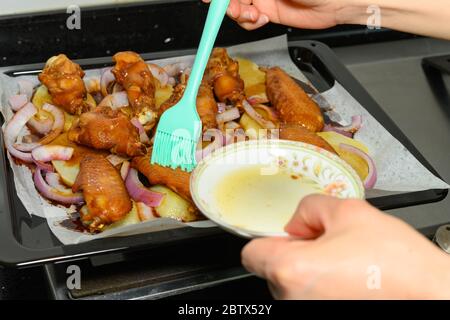 Hinzufügen von Oild zu halbgebackenen Hähnchenflügel mit Zwiebeln und Kartoffeln Stockfoto