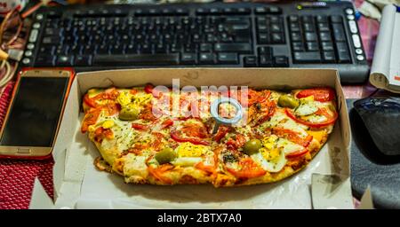 Arbeiten Sie zu Hause und liefern Sie Lebensmittel. Zuhause mit ungesunden Lebensstil. Freizeit mit Laptop und Fast Food. Fast Food Pizza und Computer auf dem Tisch. Draufsicht. Stockfoto