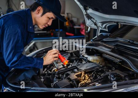 Männliche Mechaniker halten und glänzende Taschenlampe zu überprüfen, ein Auto Motor Problem Stockfoto