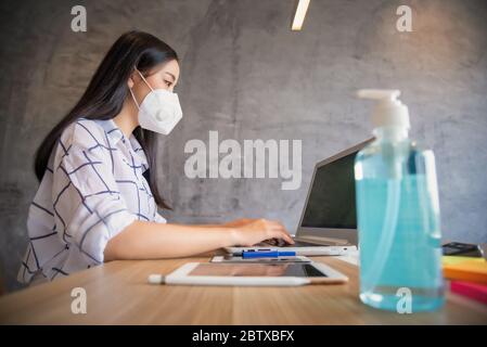 Geschäftsfrau, die von zu Hause aus mit Schutzmaske und Laptop arbeitet. Ausbruch des Coronavirus Stockfoto