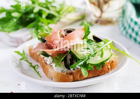 Sandwich mit Schinken, Gurke, schwarzen Oliven, Rucola und Feta auf dem Tisch. Trendkost. Stockfoto